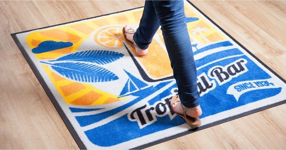 Close-up of a person walking over a vibrant tropical-themed floor mat with a colorful "Tropical Bar" logo and beach elements.